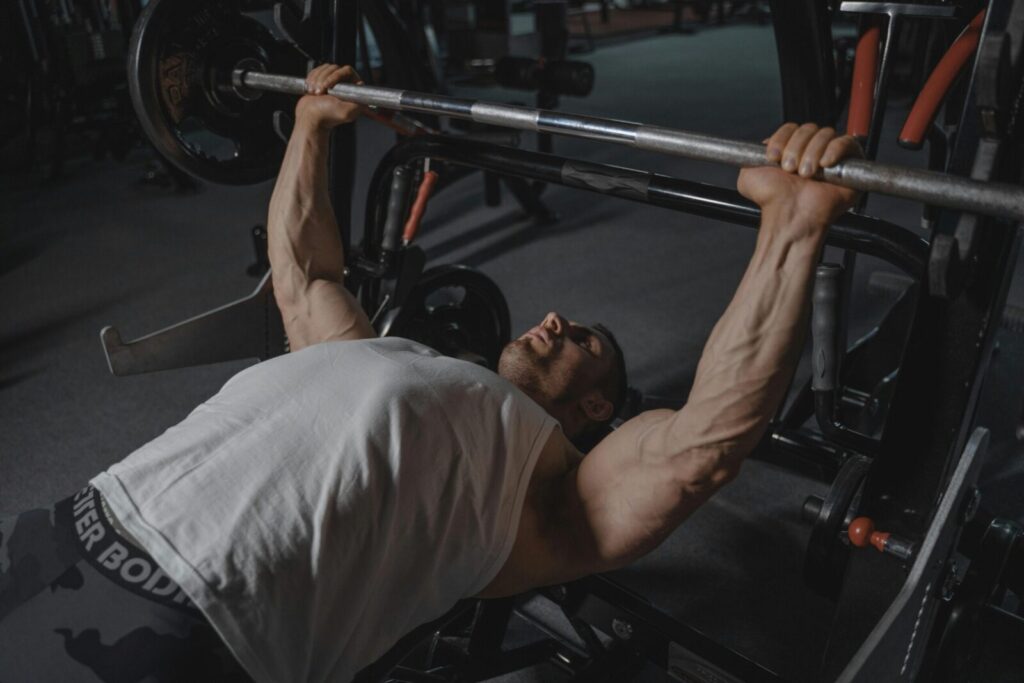 A focused man lifts heavy weights on a bench press machine in a dimly lit gym.